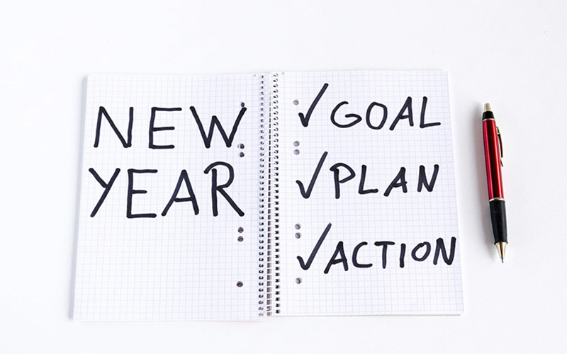 Caderno quadriculado aberto com as palavras "new year" na página esquerda e as palavras "goal", "plan" e "action" na página direita para simbolizar a análise de marketing digital que os negócios devem fazer cada ano