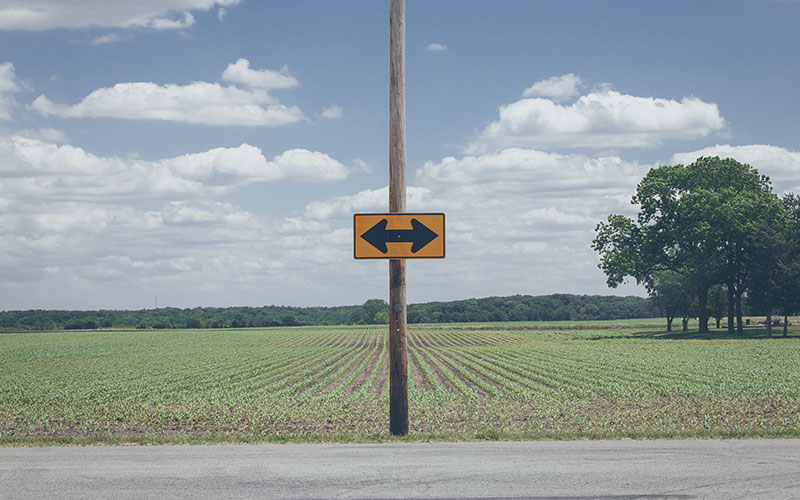 Poste de madeira com 2 setas a indicar direções opostas para exemplificar a escolha pela modalidade in-house ou outsource no desenvolvimento do marketing digital do seu negócio