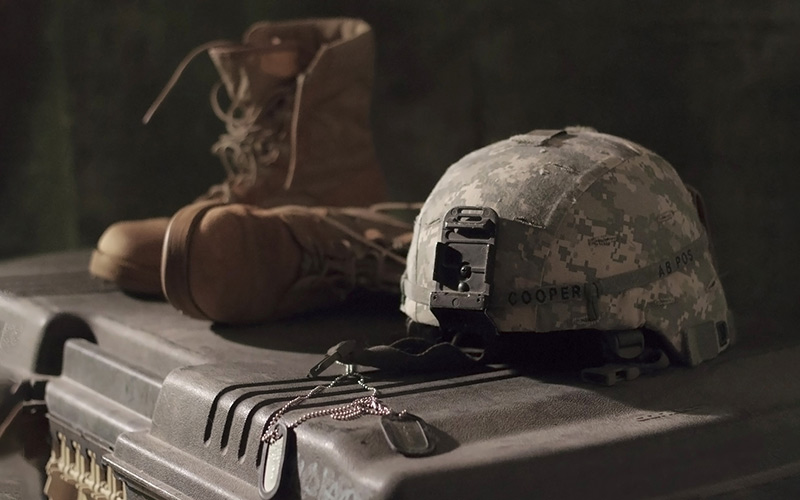 Um capacete, botas e chapas de identificação militares sobre uma caixa de armamento para representar a guerra online no plano digital